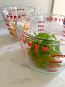 glass measuring cup with basil and cheese